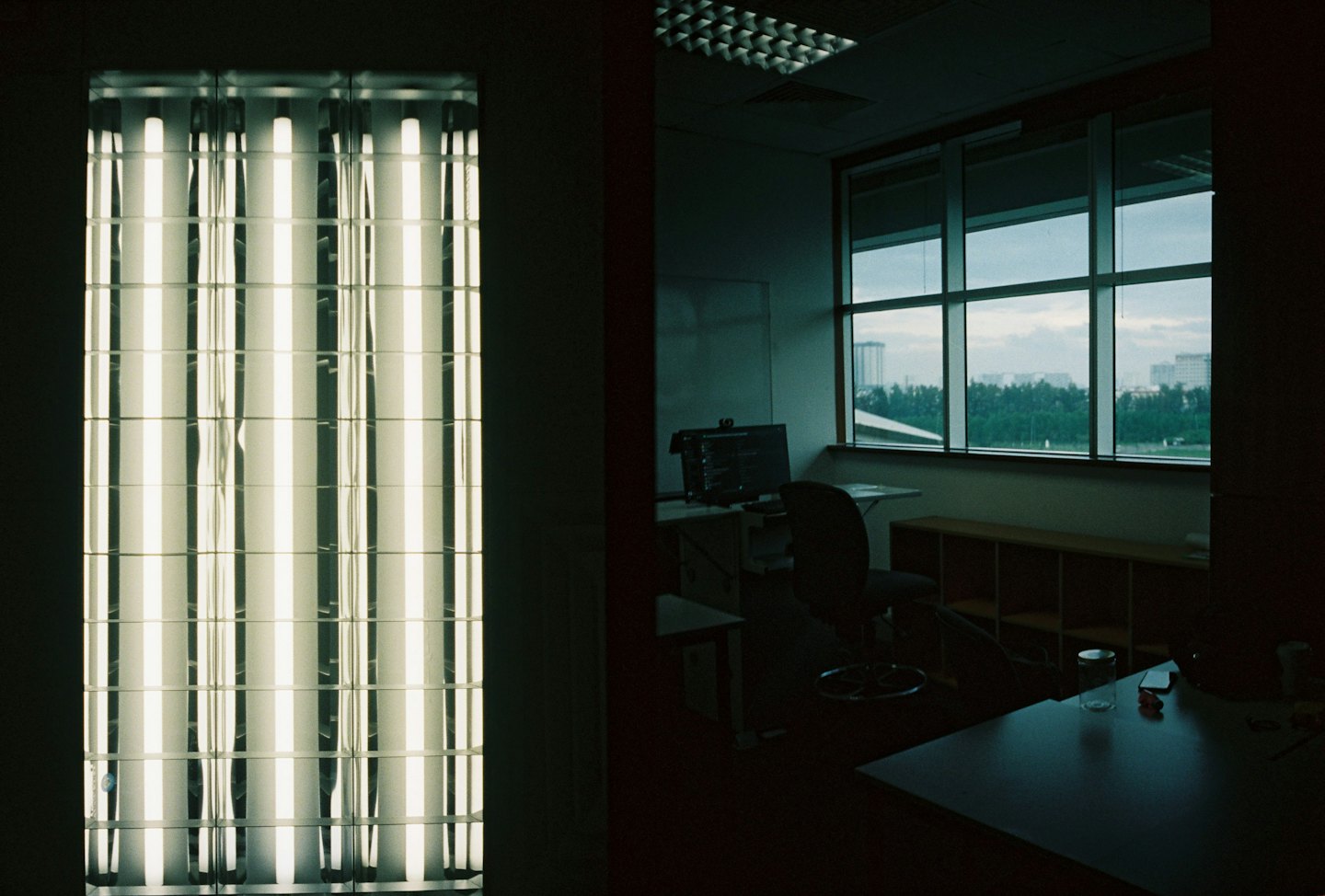 Fluorescent light fixture illuminates a workspace with city views.